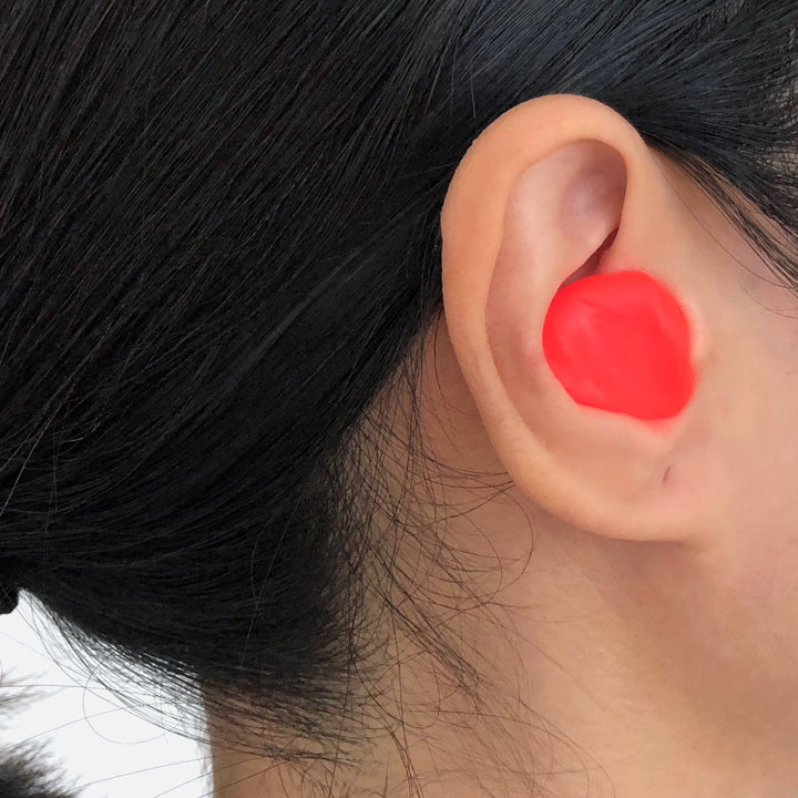 Close-up of a orange Mack's Silicone Earplug molded into the ear, showcasing a secure and custom fit.