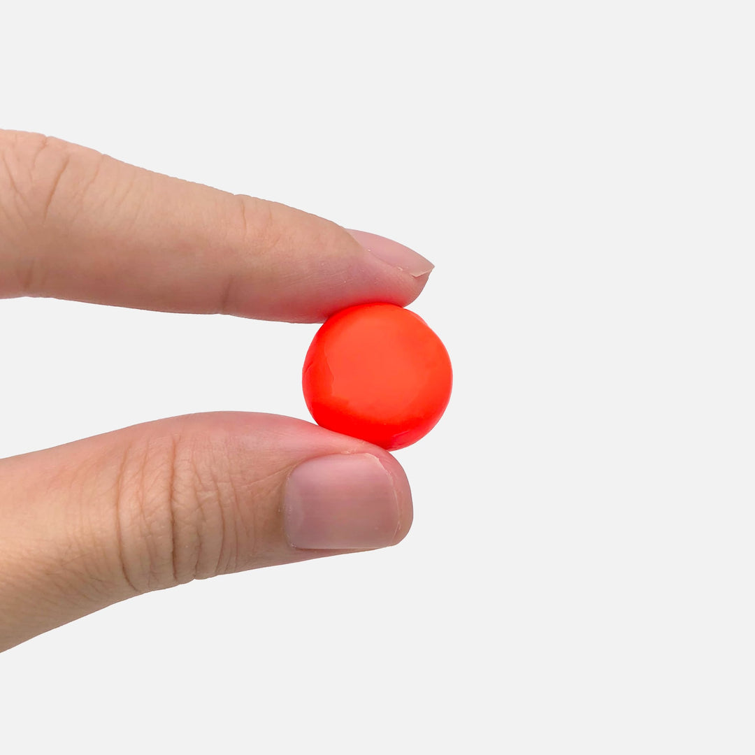 Hand holding an orange Mack's Silicone Earplug molded into a ball, ready for a custom fit.