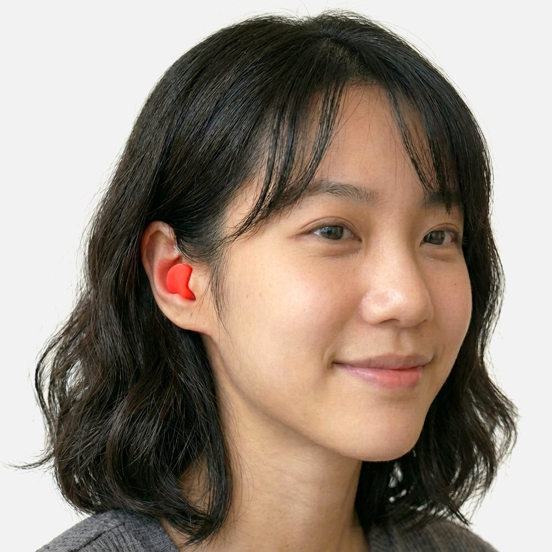 Model wearing Mack's Snore Mufflers silicone putty earplug in ear, showing soft moldable red silicone fit