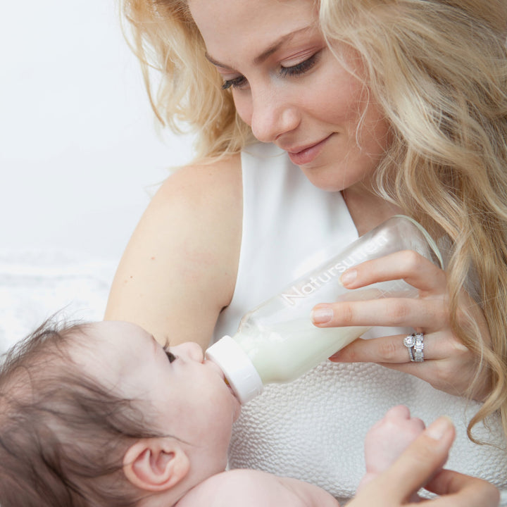 Mother feeding baby with Natursutten baby bottle featuring anti-colic valve.