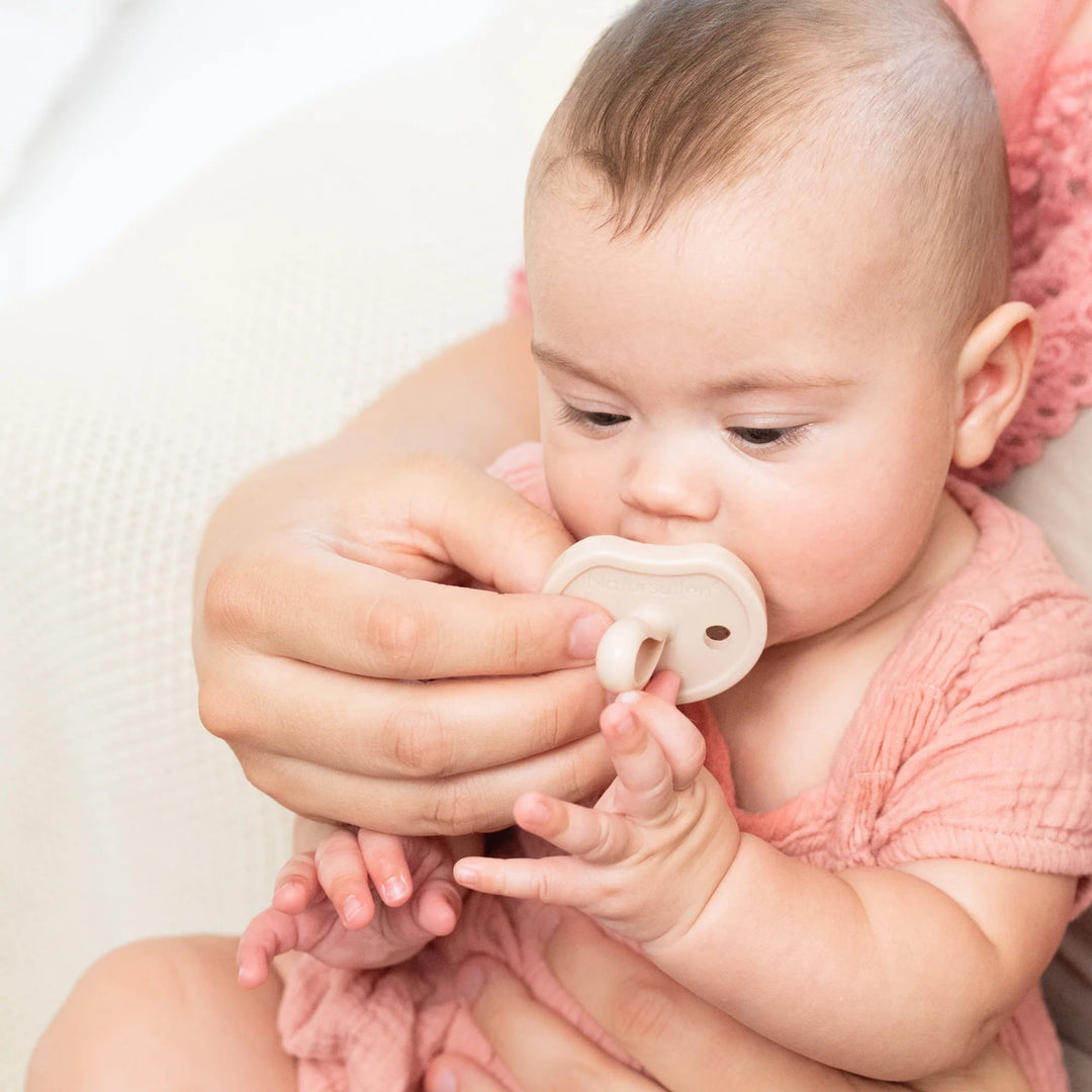 Baby using Natursutten Butterfly Orthodontic Pacifier in Pale Blush, held by a parent for soothing comfort.